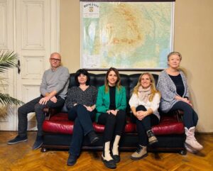 Five people sitting on a sofa, looking into the camera.